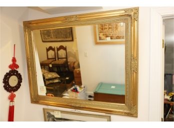 GOLD FRAME MIRROR AND RED WALL HANGING NEXT TO IT.