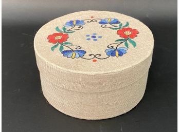 A Fabric-Covered Storage Box With Embroidered Floral Wreath On Lid