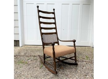 An Antique High Back Rocking Chair With Cushioned Seat