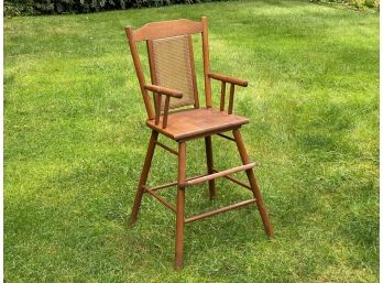 A Vintage High Chair With A Caned Back Rest