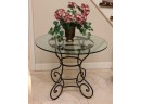 38 INCH ROUND GLASS TABLE ON ORNATE CURVED WROUGHT IRON BASE INCLUDES FAUX FLORAL DISPLAY