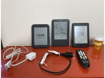 Assortment Of Tablet Reading Devices Featuring Two Amazon Kindles And A Nook Reader, Plus Charger And More
