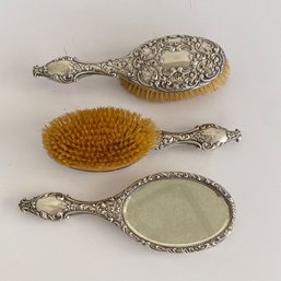 (2) Ornate Silver Brushes And (1) Ornate Silver Hand Mirror